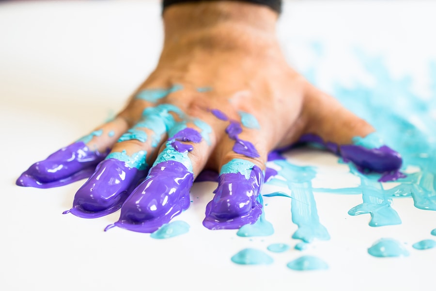 A hand moving through blue and purple paint